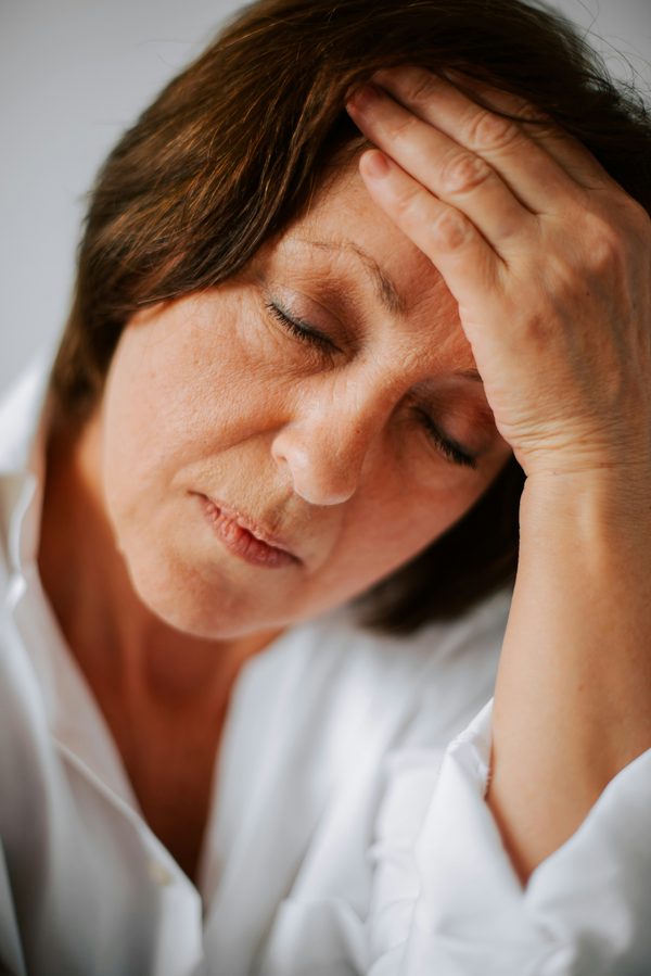 Périménopause, ménopause et hormonothérapie à la Clinique Synergek. Femme dans la cinquantaine, les yeux fermés, la main sur le front - symptômes de la périménopause et de la ménopause - Clinique Synergek